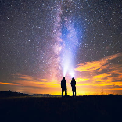 siluetas de dos personas contemplando las estrellas en un prado